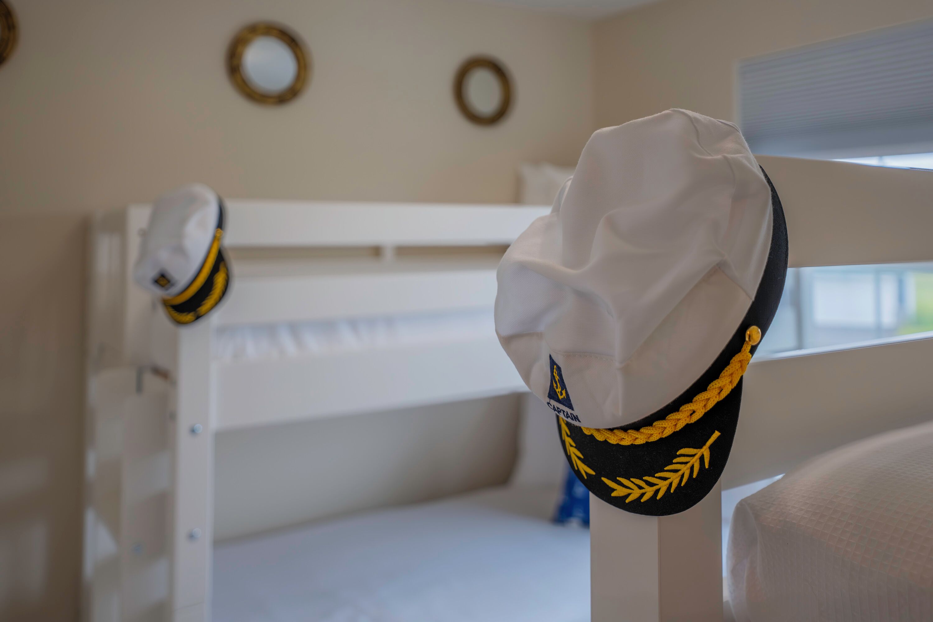 A bunk bed with a white headboard and a white pillow. A white sailor hat is hanging on the headboard.