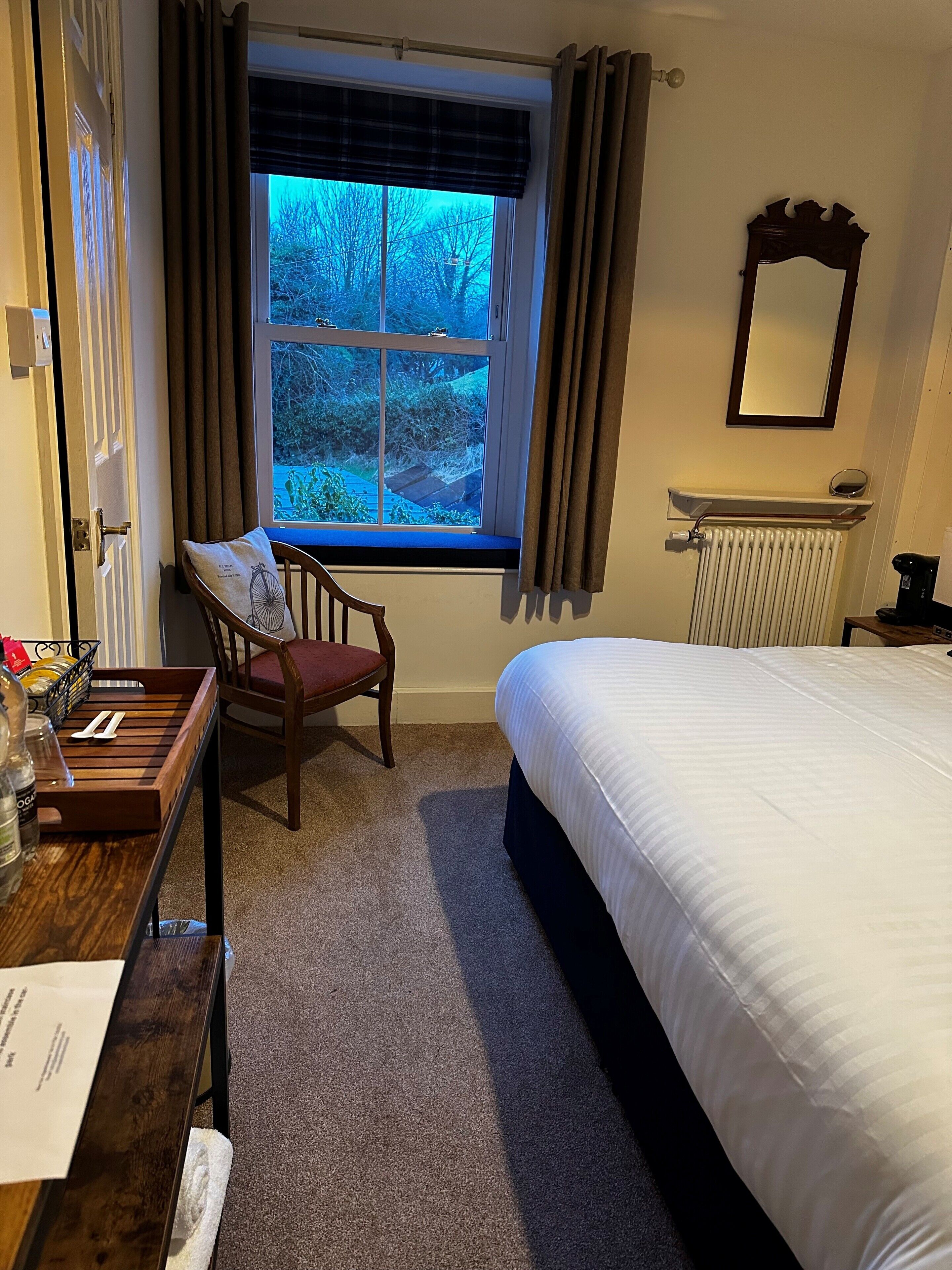 Une chambre à coucher avec un lit, une chaise, une fenêtre avec des rideaux, un radiateur et un miroir au mur.