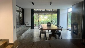 A modern dining area with a wooden table and chairs, a stone floor, and a view of greenery through large windows. - Bryanston Luxurious 4-Bed Villa (Sandton)