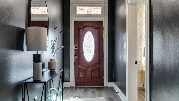 A dark hallway with a wooden door, a mirror, and a lamp on a console table.