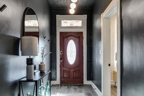 Un pasillo oscuro con una puerta de madera, un espejo y una lámpara sobre una consola.