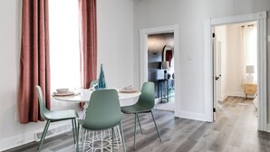 A dining area with a white table, two green chairs, and a window with pink curtains.