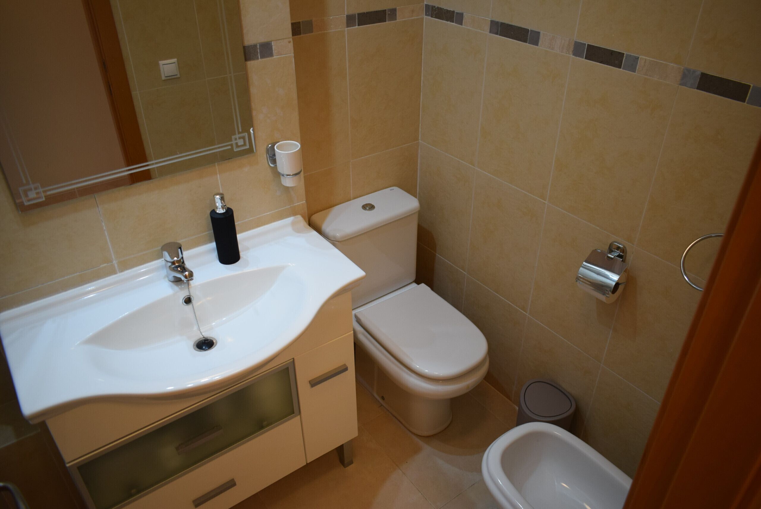 A bathroom with a sink, toilet, bidet, and mirror.
