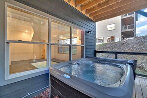 Ein Whirlpool auf einer Holzterrasse mit großen Fenstern und Blick auf ein modernes Gebäude.