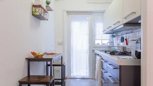 A narrow kitchen with a dining table and chairs, a built-in oven, and a window with sheer curtains.