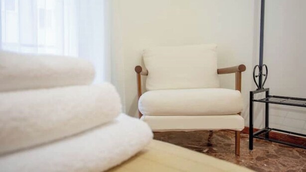 A white armchair with wooden legs in a room with a marble floor.