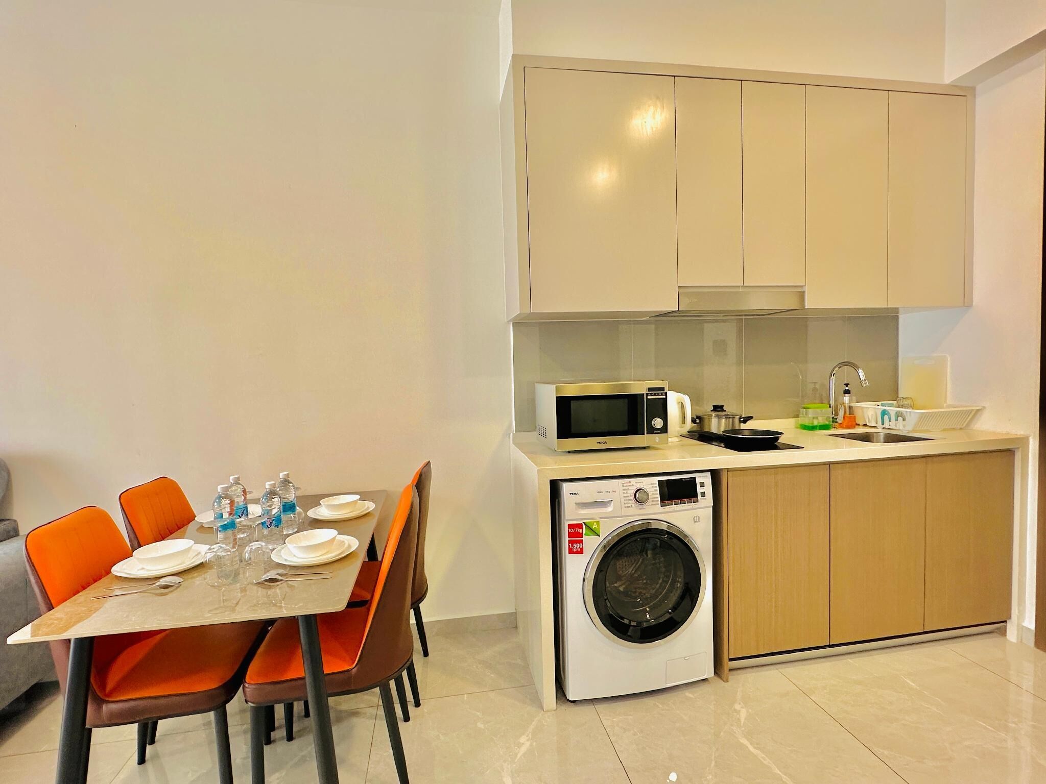 Une cuisine compacte équipée d’un four à micro-ondes, d’un lave-linge, d’un évier et d’un coin repas avec des chaises et une table pour deux personnes.