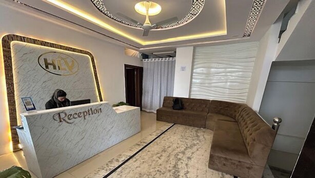 Uma área de recepção com um balcão de mármore identificado com a palavra "Reception", um ventilador de teto e um sofá seccional marrom.