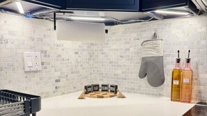 Uma cozinha com bancada branca, coifa preta e backsplash revestido de azulejos.