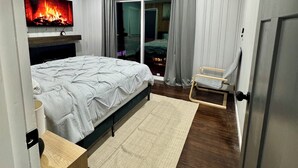 Quarto moderno com cama, TV fixada na parede, mesinha e porta de correr para uma varanda.