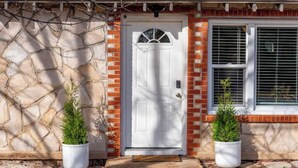 Une maison avec une façade en pierre, une porte blanche et deux plantes en pot.