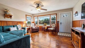 Un salon avec un canapé vert, un meuble en bois et un ventilateur de plafond.