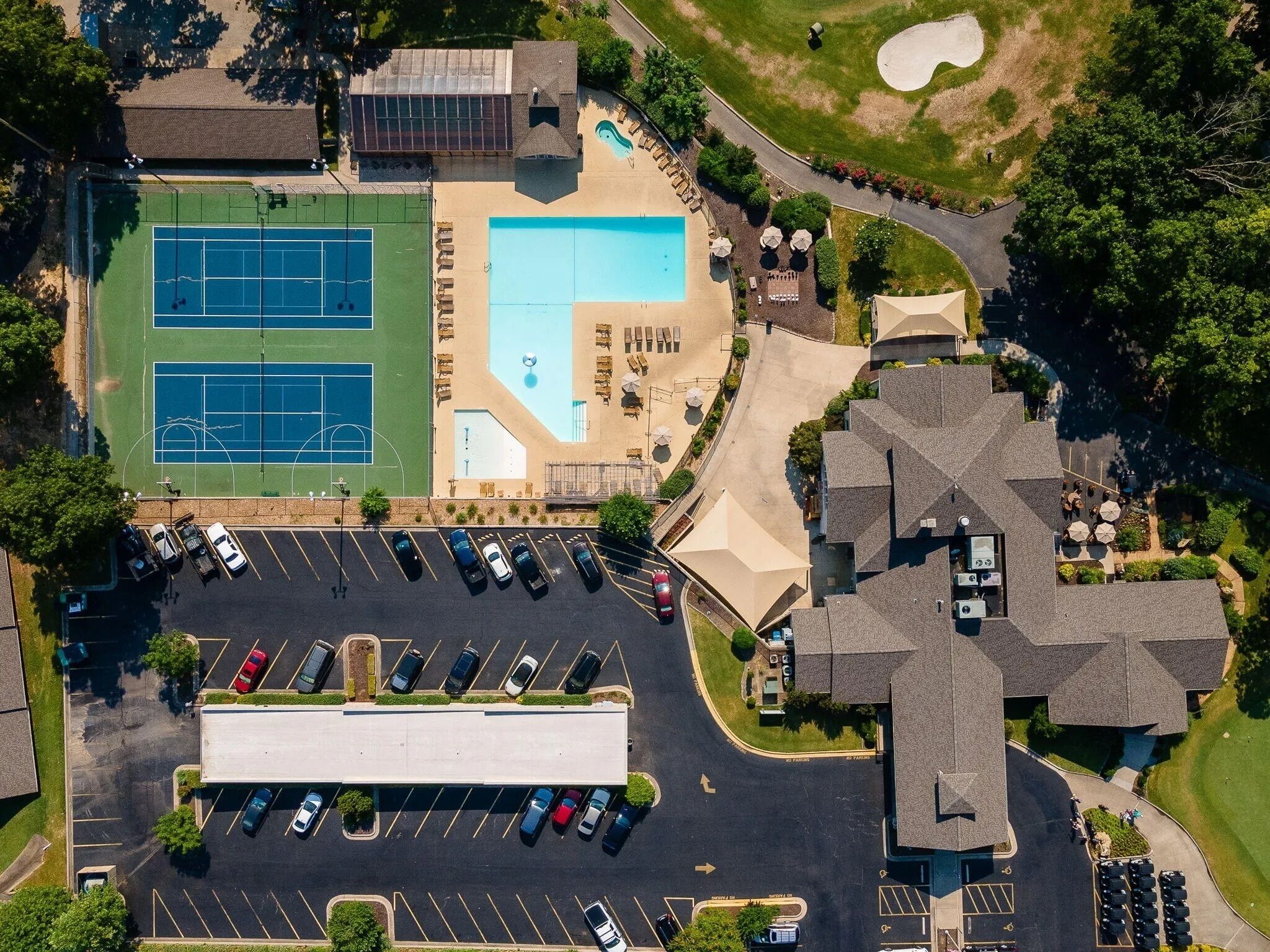An aerial view of a property with a tennis court, a swimming pool, and a parking lot.