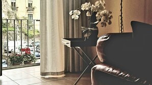 Un salon moderne avec un canapé en cuir, une table d’appoint ornée d’un vase de fleurs blanches et une vue sur le paysage urbain, visible à travers une grande fenêtre.
