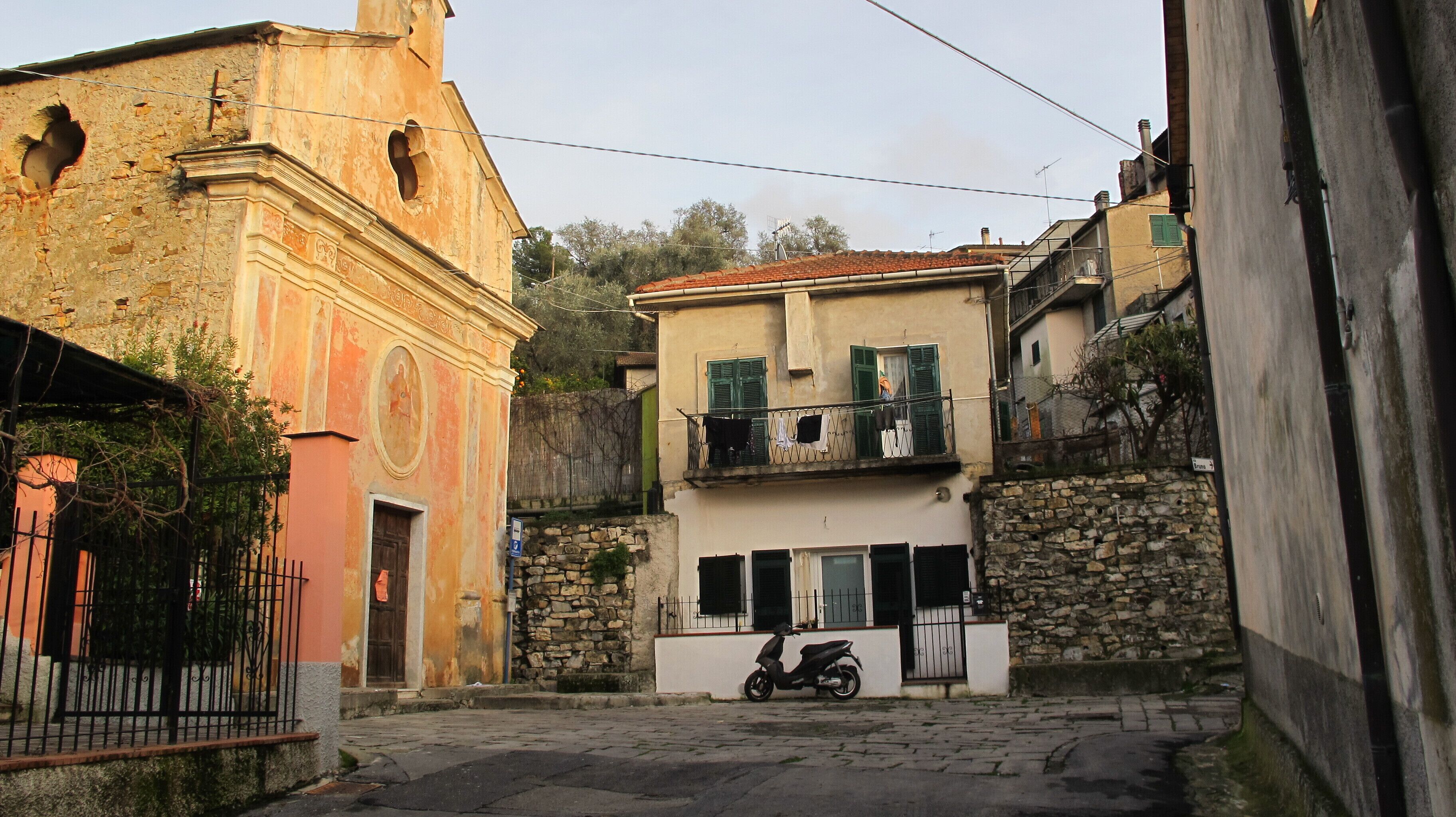 A narrow street with a historic building featuring a bell tower and a white building with a balcony.