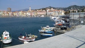A harbor with boats docked, a waterfront promenade, and a cityscape with buildings and a hill in the background. - Ligurian rustico, surrounded by olive groves, 10 minutes from the sea. (Imperia)
