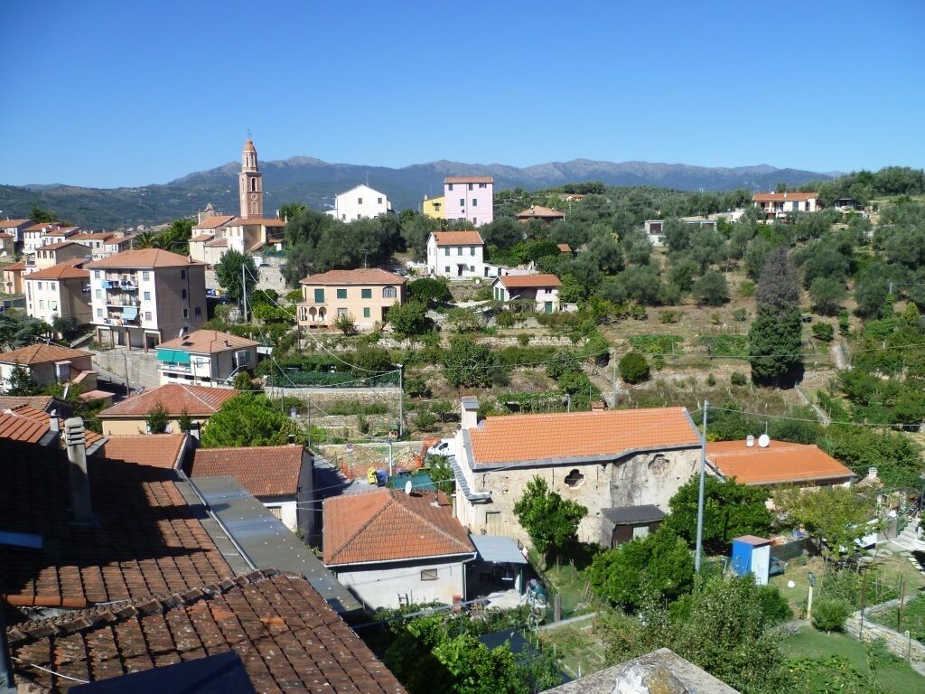 A hillside village with traditional buildings, a church tower, and a mountainous backdrop.