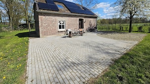 Edificio de ladrillo con paneles solares en el techo, un patio con mesa y sillas, y un área de césped con árboles.