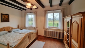 Un dormitorio con cama de madera, dos ventanas con cortinas, un radiador y un armario de madera.
