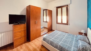 Un dormitorio con cama, armario de madera, televisión, ventilador de techo y ventana con persianas.