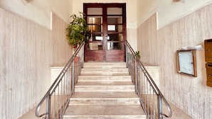 Una escalera de mármol con barandillas de metal que conduce a una puerta de madera con paneles de vidrio.