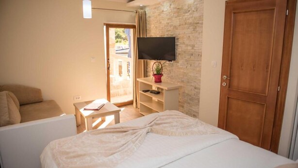 A bedroom with a bed, a TV mounted on the wall, a wooden door, and a small table with a plant. - Ground Floor Apartment, Private Beach and Seaview (Tivat)