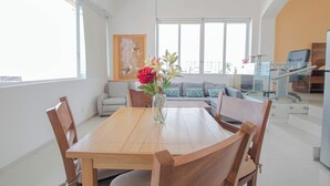Een eethoek met een houten tafel en stoelen, een vaas met bloemen en een bank met gekleurde kussens.