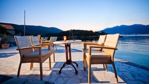 Eine Terrasse mit Korbmöbeln und einem Tisch, mit Blick auf ein Gewässer und Berge.