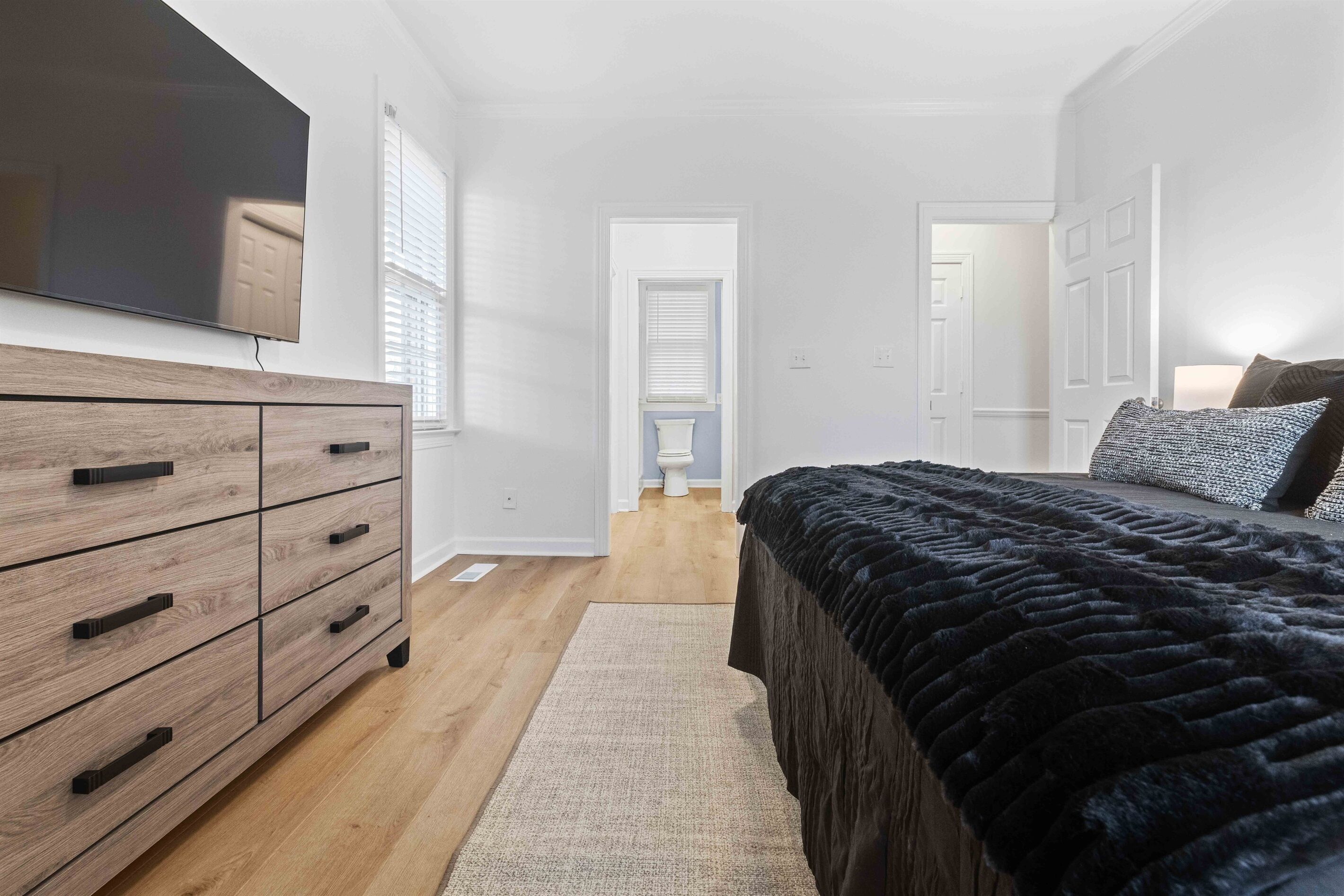 Een slaapkamer met een groot bed, een houten dressoir, een flatscreen televisie en een deur naar een andere kamer.