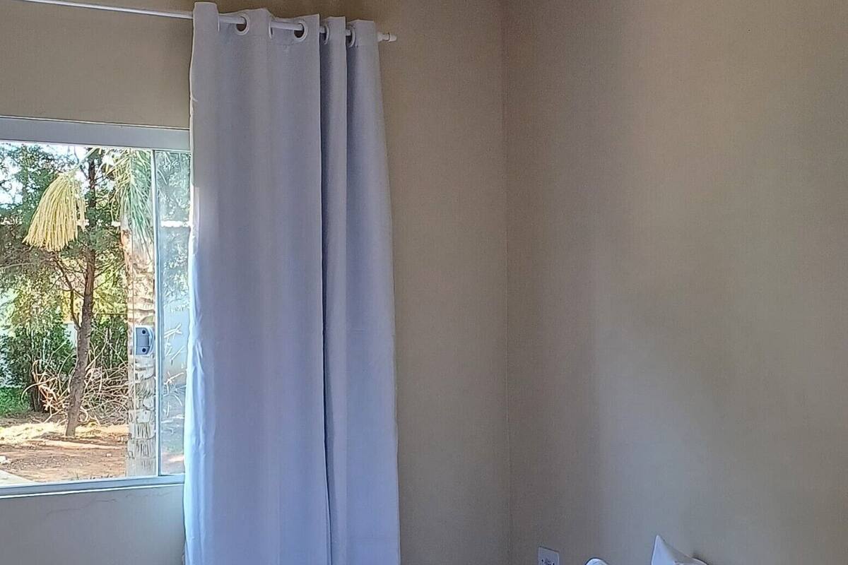 Une chambre à coucher avec un lit, une fenêtre avec des rideaux, une table de chevet avec des serviettes et un luminaire au plafond.
