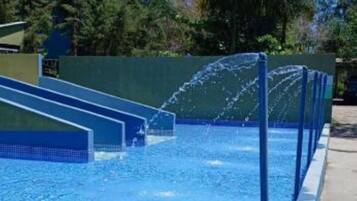 Piscina com água azul cristalina, rodeada por um deck de concreto e palmeiras.