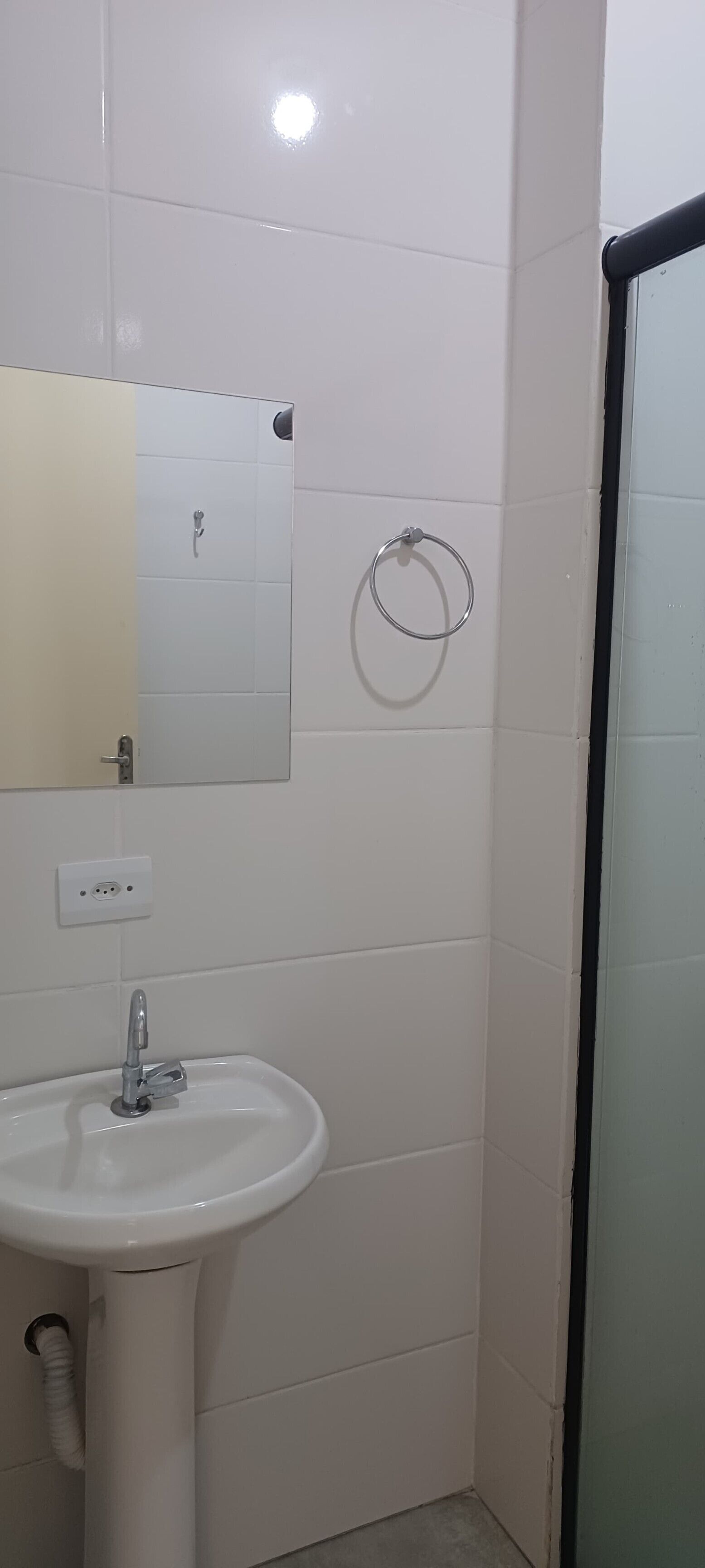 A bathroom with a white sink, a mirror, a towel ring, and a shower area.