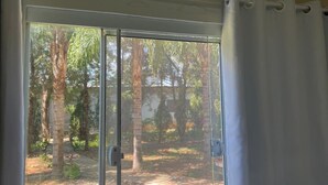 Une pièce dotée d’une grande fenêtre, d’un appareil de climatisation installé au-dessus, et offrant une vue sur un jardin avec des arbres et de la pelouse.