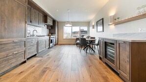 A modern kitchen with wooden cabinets, a dining area with a table and chairs, and large windows providing natural light.