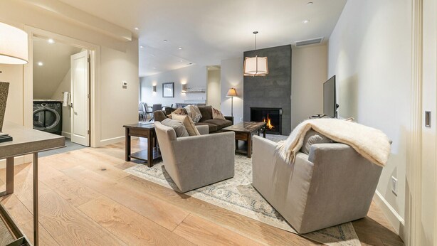 A spacious living room with a fireplace, a dining area, and a kitchen in the background.