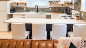 Una cocina moderna con una isla central, iluminación colgante y un comedor con sillas acolchadas.
