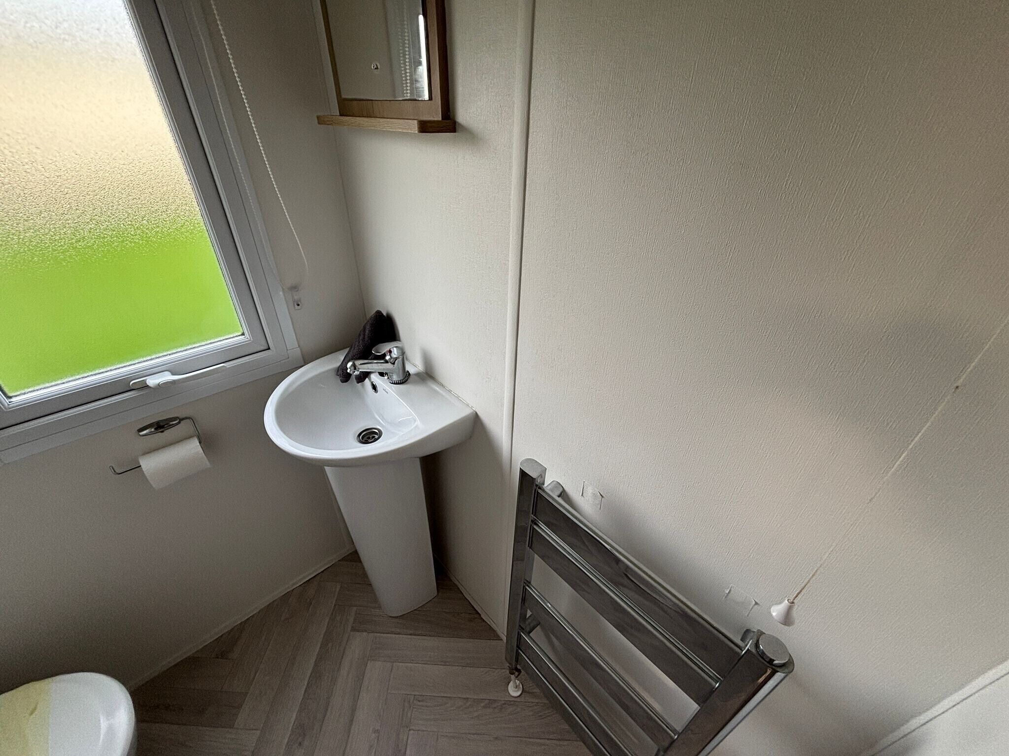 A small bathroom with a white sink, a window, and a radiator.