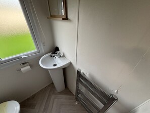 A small bathroom with a white sink, a window, and a radiator. - Eyemouth - Caravan - Sleeps 4 - Pet Friendly (Eyemouth)