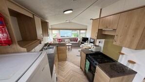 Una cucina compatta con fornelli, lavello e pensili in legno. C'è un'area pranzo con tavolo e sedie, e una finestra che offre vista sull'esterno.