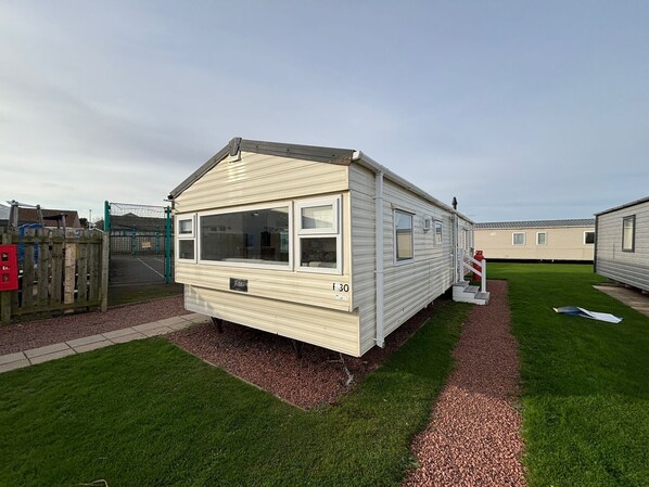 Une maison mobile de plain-pied, dotée d’un toit à deux versants, de grandes fenêtres et d’un petit porche.
