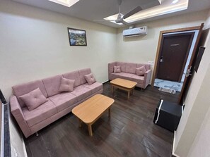 Un salon avec deux canapés et une table basse, un ventilateur de plafond et un appareil de climatisation.