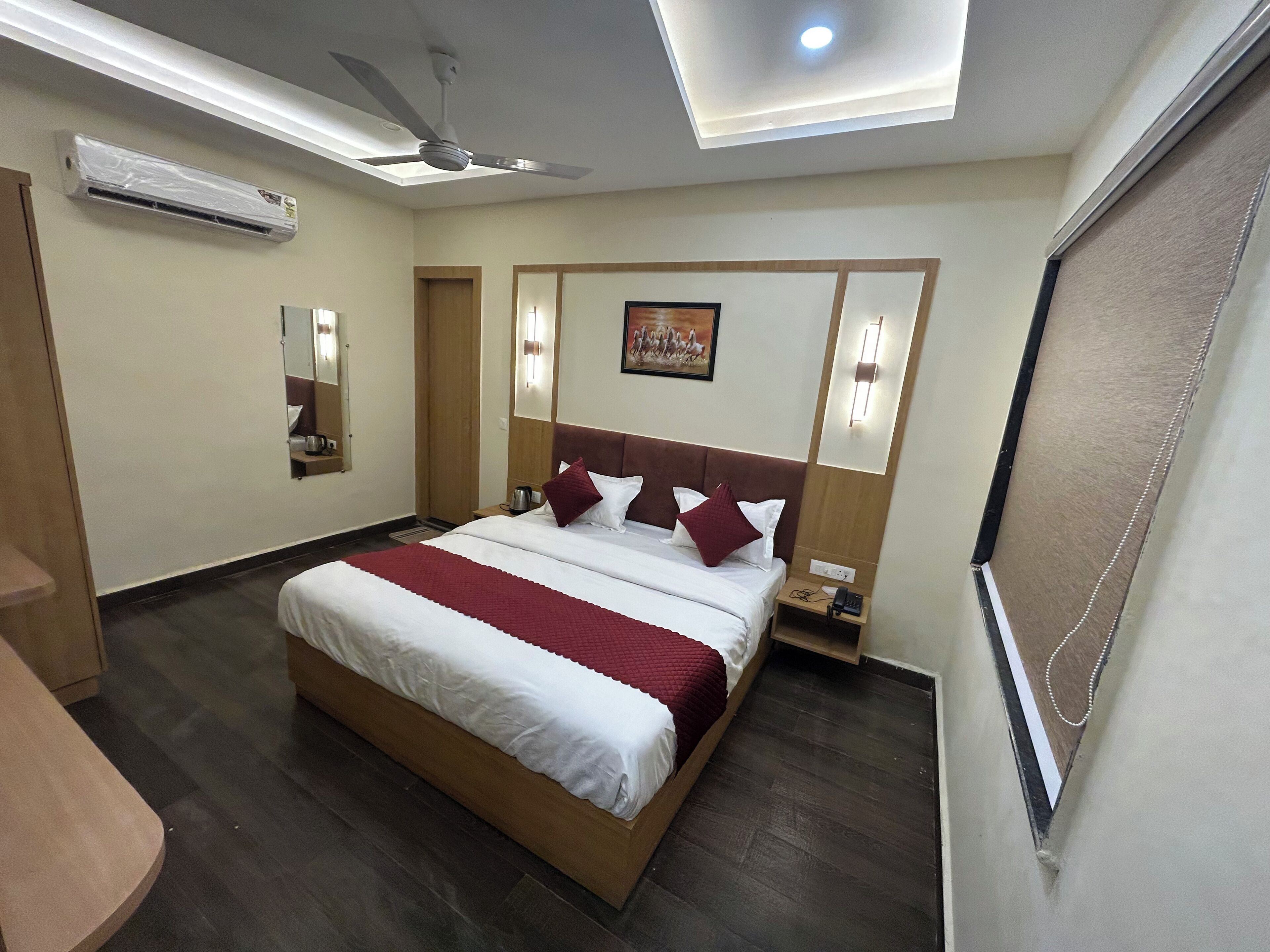 Une chambre d’hôtel avec un grand lit, un ventilateur de plafond, un appareil de climatisation, une table de chevet avec un téléphone et un luminaire fixé au mur.