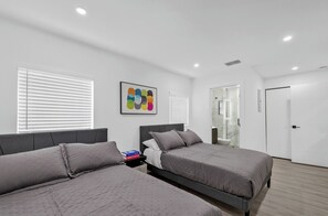 A modern bedroom with two beds, a bathroom, and a door leading to another room.