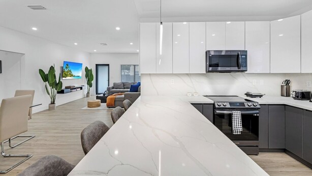 A modern kitchen with white cabinets, a large island, and stainless steel appliances. - Design Dist Living:Pool,Basketball CourtandNespresso (Miami)
