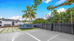 A basketball court with a pool table, a fence, and a palm tree. - Design Dist Living:Pool,Basketball CourtandNespresso (Miami)