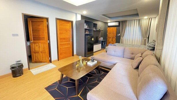 A modern living room with a sofa, a coffee table, and a kitchen area with cabinets and a refrigerator. - Marin House Pattaya (Pattaya)