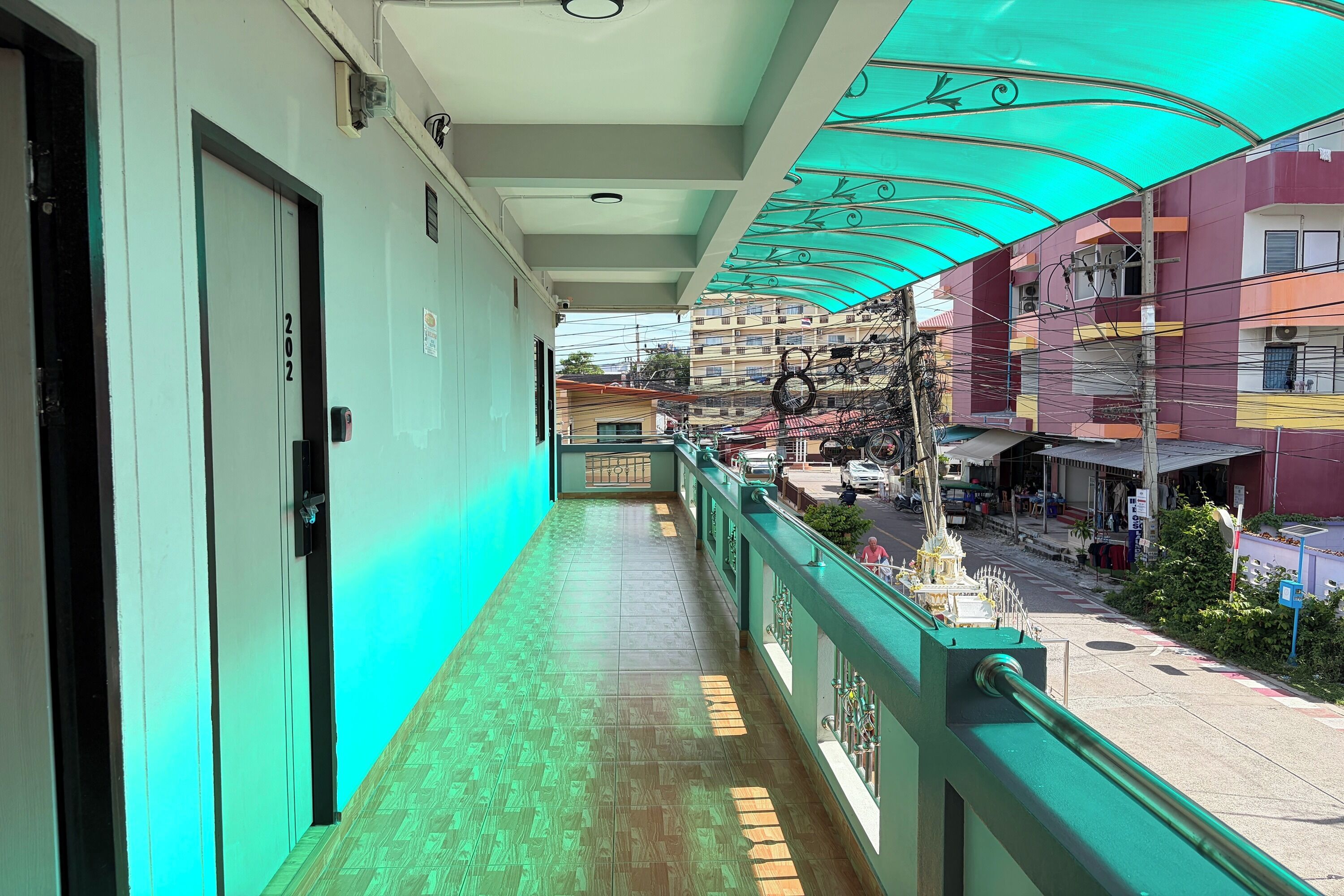 A corridor with a green railing, a door labeled '202', and a view of the street below.