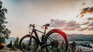 A mountain bike parked on a grassy hill with a scenic view of a town and hills in the background. - Oas Finnerödja (Finnerödja)