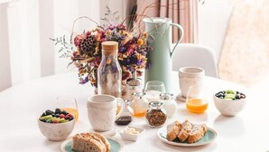 A breakfast table with various food items, a pitcher, and a vase of flowers. - Oas Finnerödja (Finnerödja)