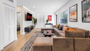 A modern living room with a sectional sofa, a flat-screen TV, a zebra-patterned rug, and a minimalist design. - Design Dist villa:Pool,HotTub,billardandNespresso (Miami)